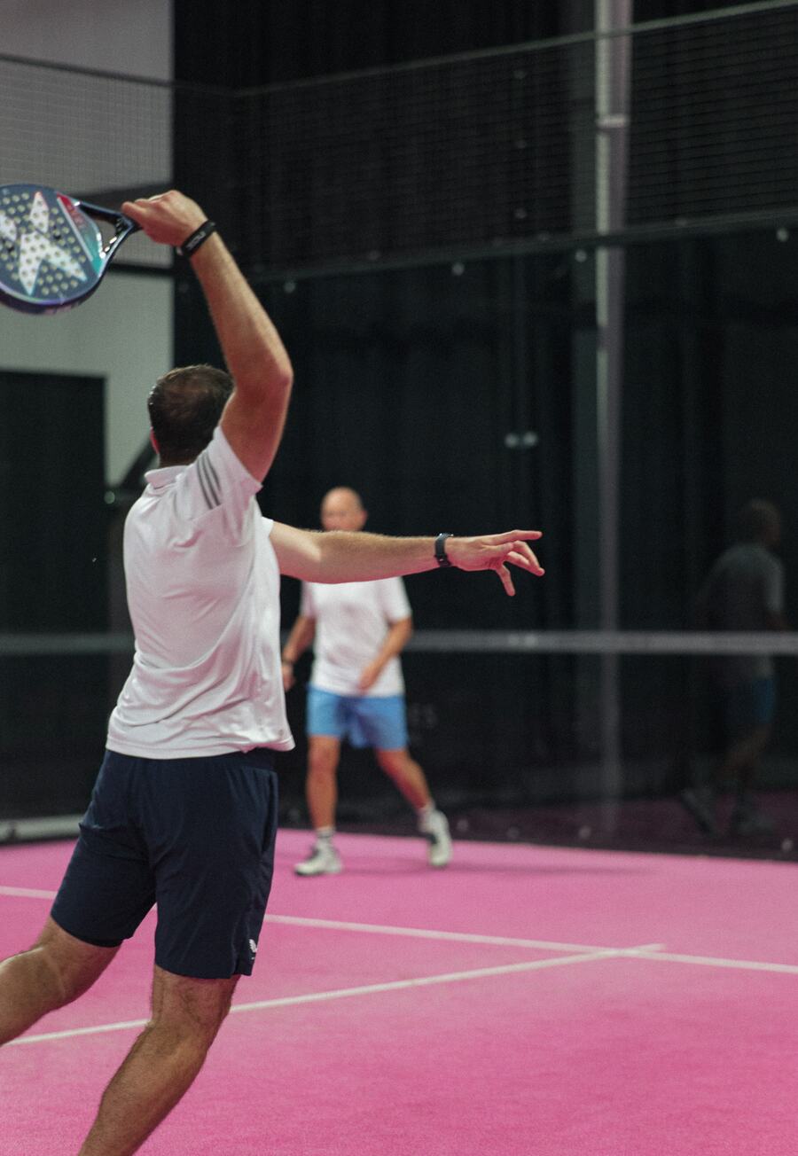 A player in white mid-smash while his opponent watches from the back of the pink court.