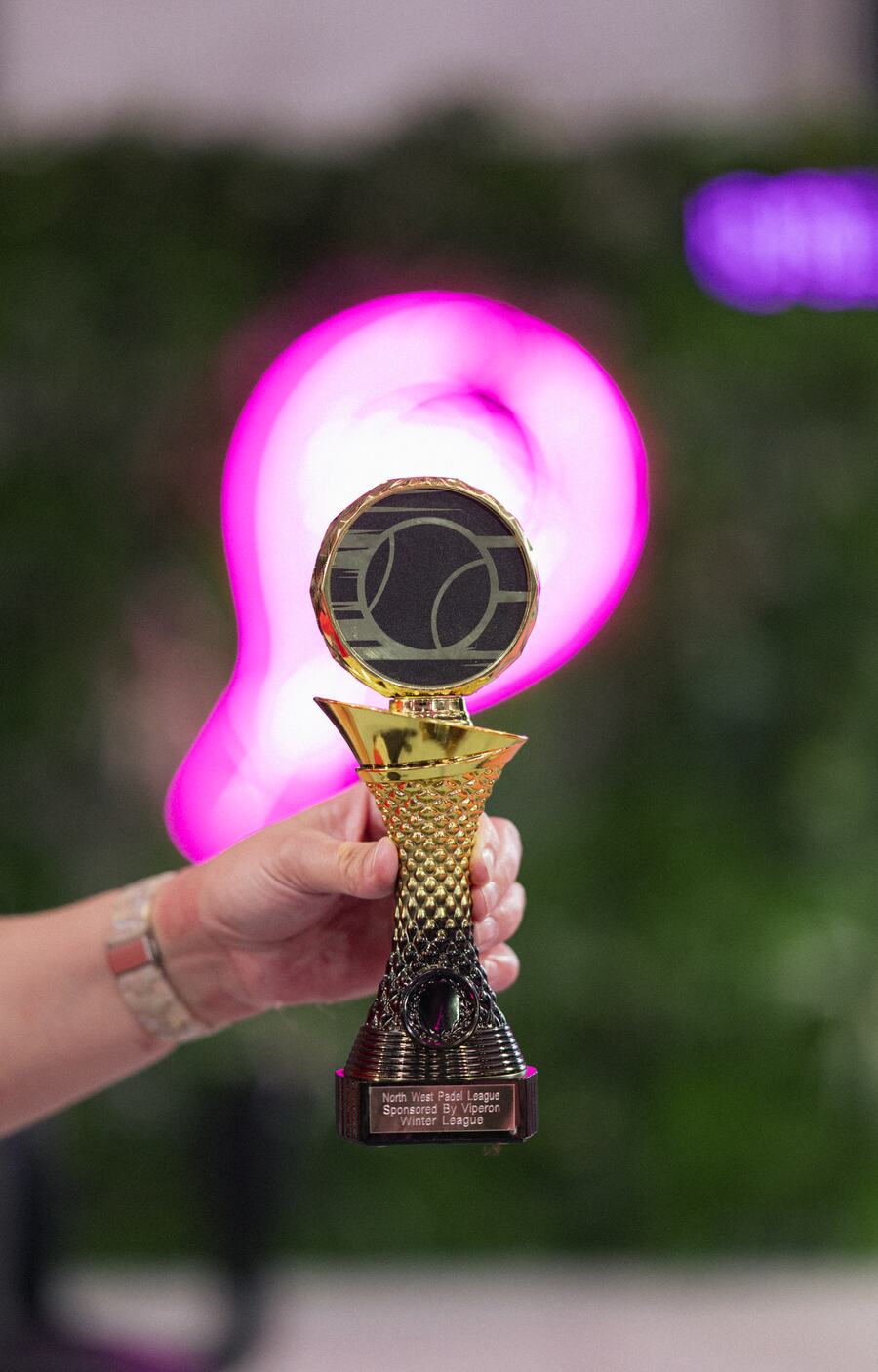 A hand holding up the gold North West Padel League winter league trophy.