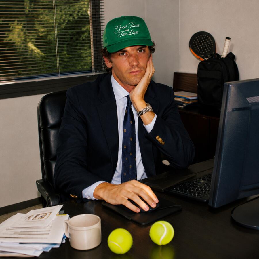 A man in a suit and a green PSF cap sitting at an office desk with two tennis balls in front of him.