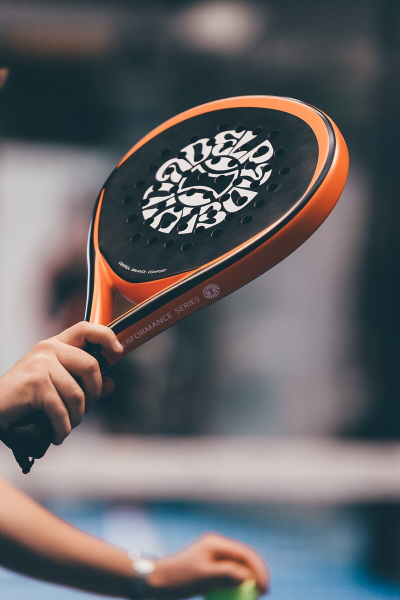 An orange and black Vida Del Padel racket held up in front of the camera.