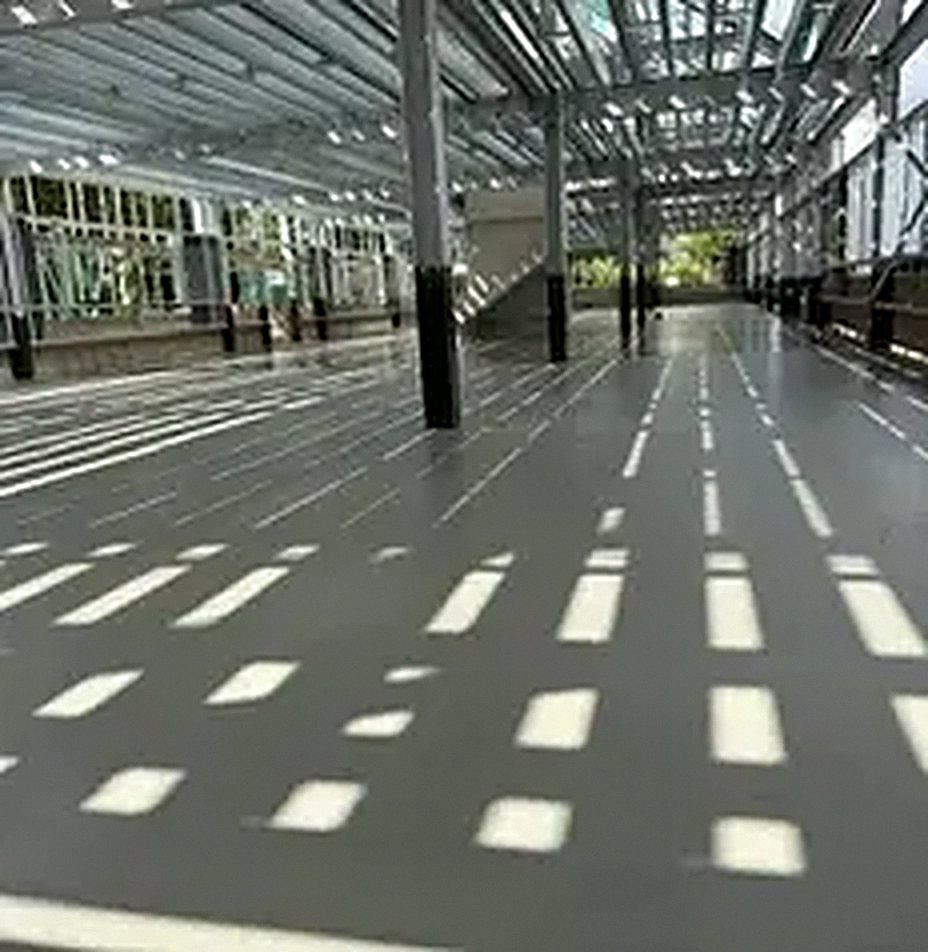 A long, smooth grey floor under a glass and steel canopy, with bright reflections of the roof lights running along it.