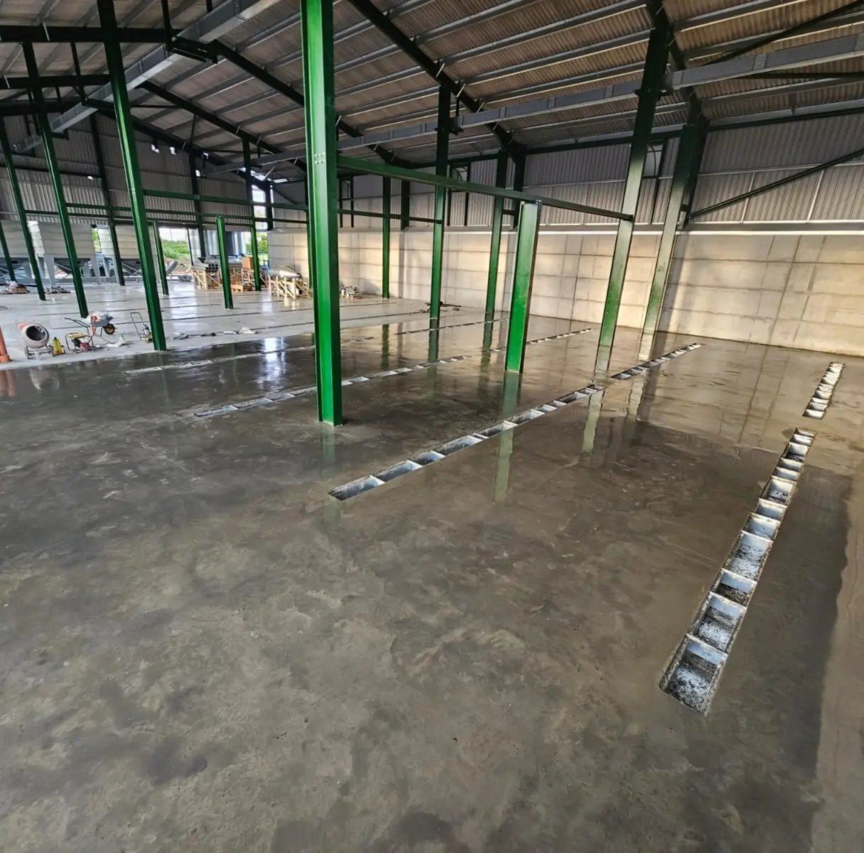 A large industrial building under construction with green steel columns and a fresh concrete floor.