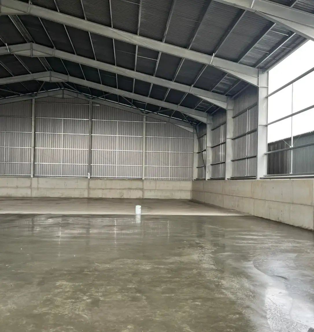 A big steel-framed shed with a smooth concrete floor and tall windows along one wall.