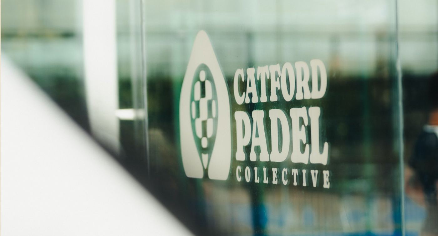 The Catford Padel Collective logo on a glass court wall