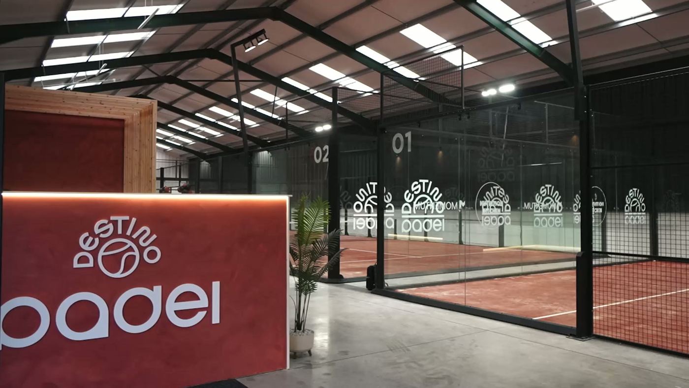 A terracotta-coloured reception desk with the club logo beside a row of indoor padel courts