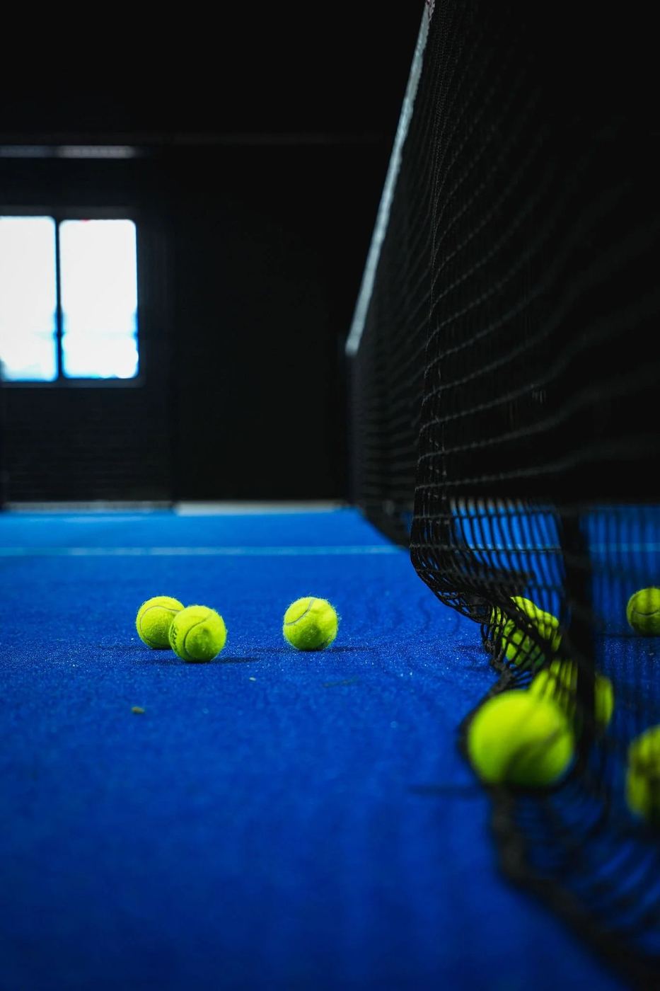 Yellow padel balls on blue turf beside the net