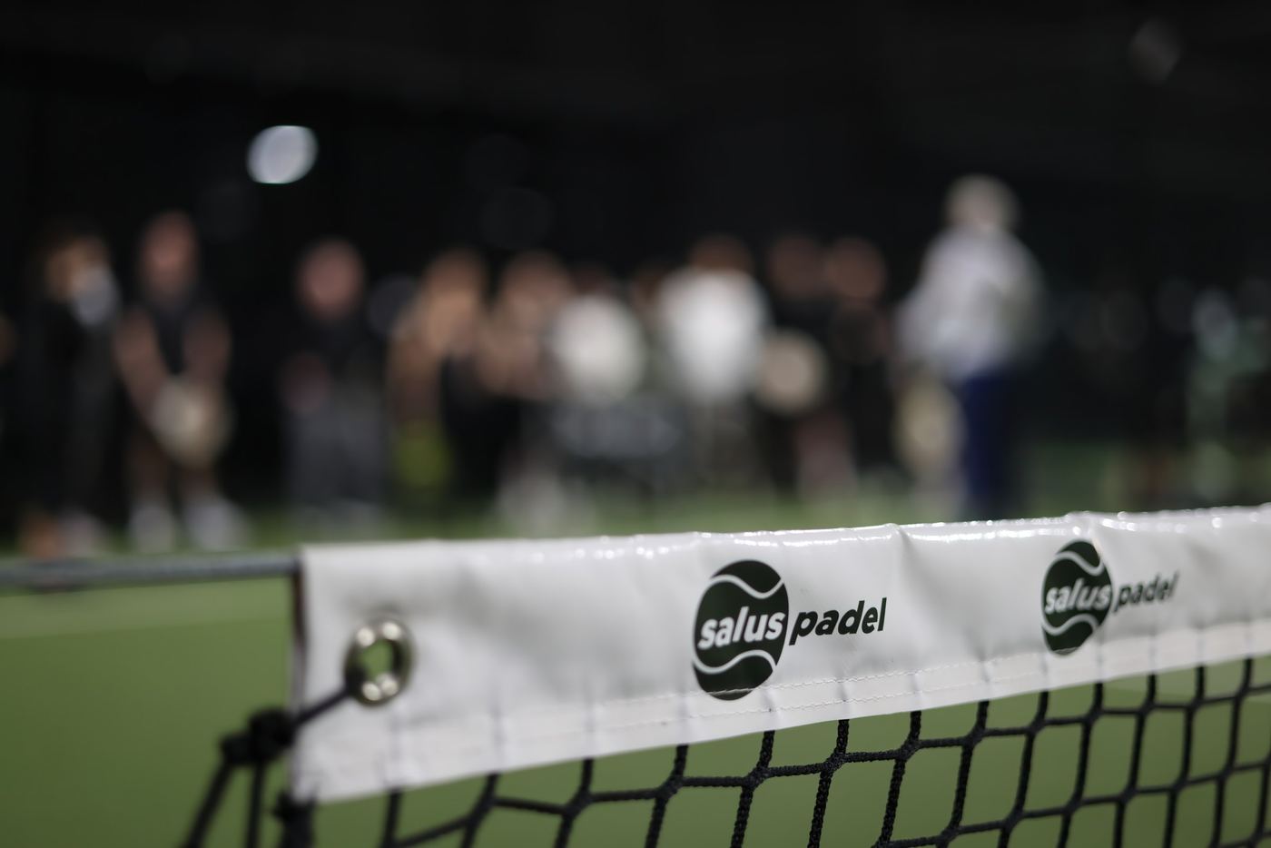 Close view of a padel net with the Salus Padel logo on the net band and blurred spectators behind