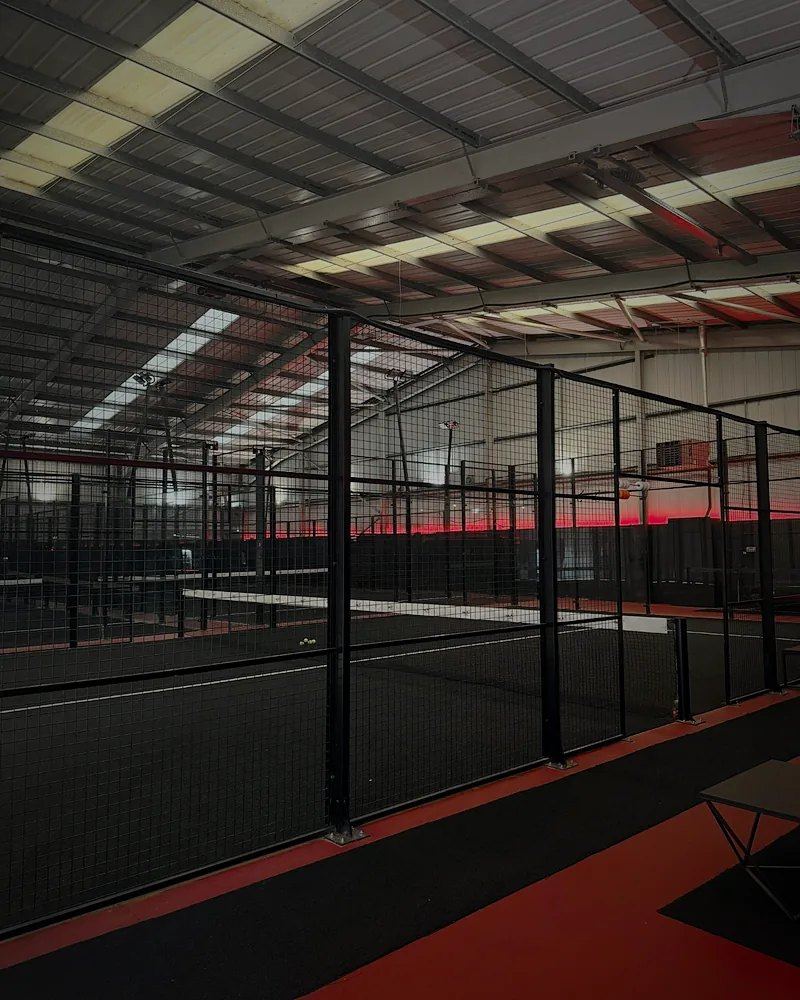 Indoor black-turf padel courts lit by a red LED strip along the walls